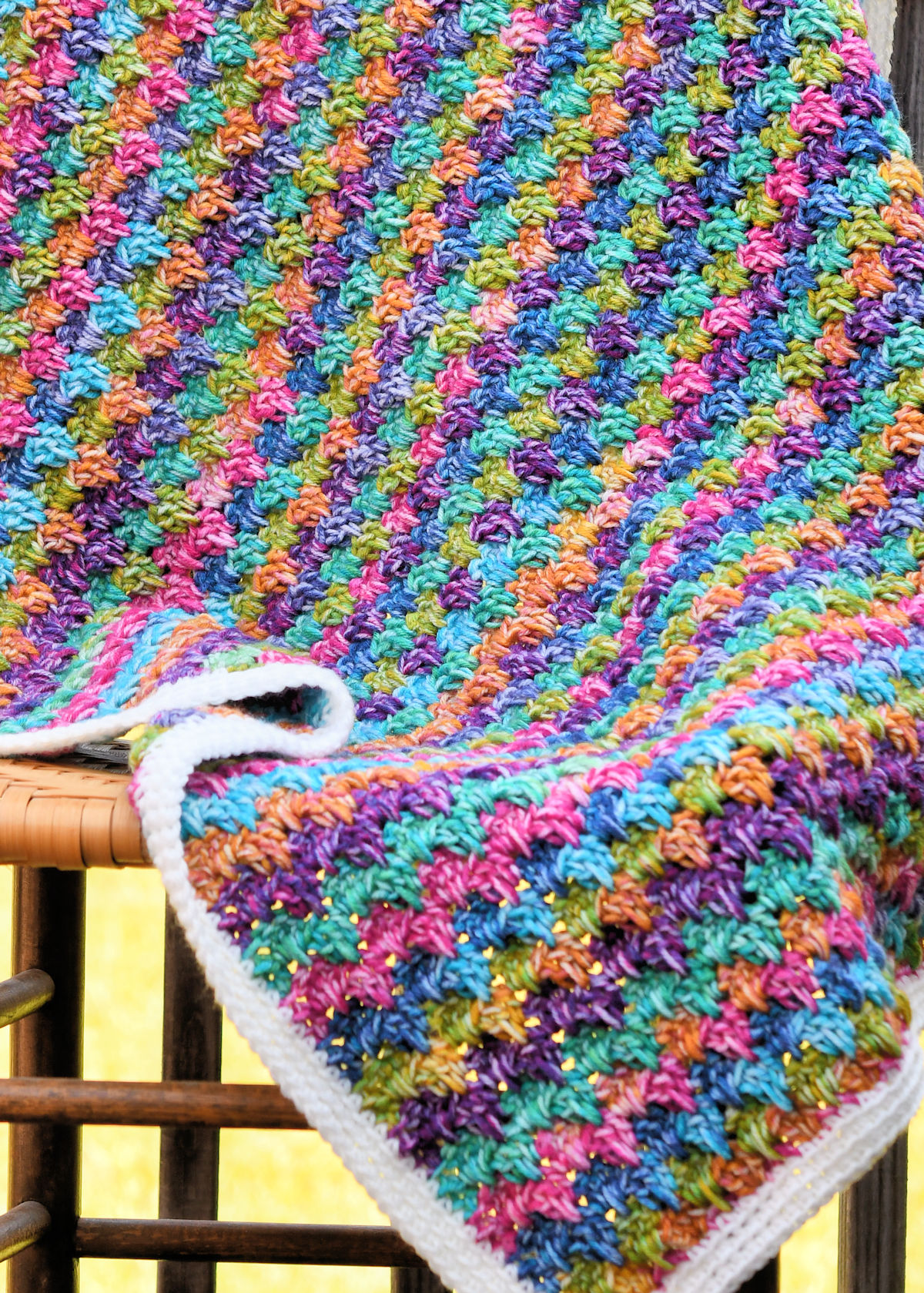 Bright striped crochet baby blanket draped over a wooden chair.