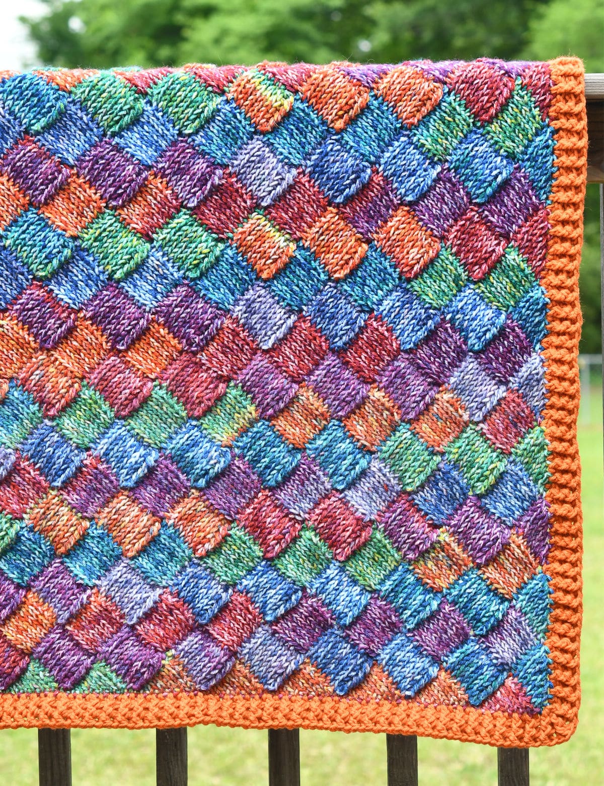 Bright and colorful entrelac blanket on railing outside.