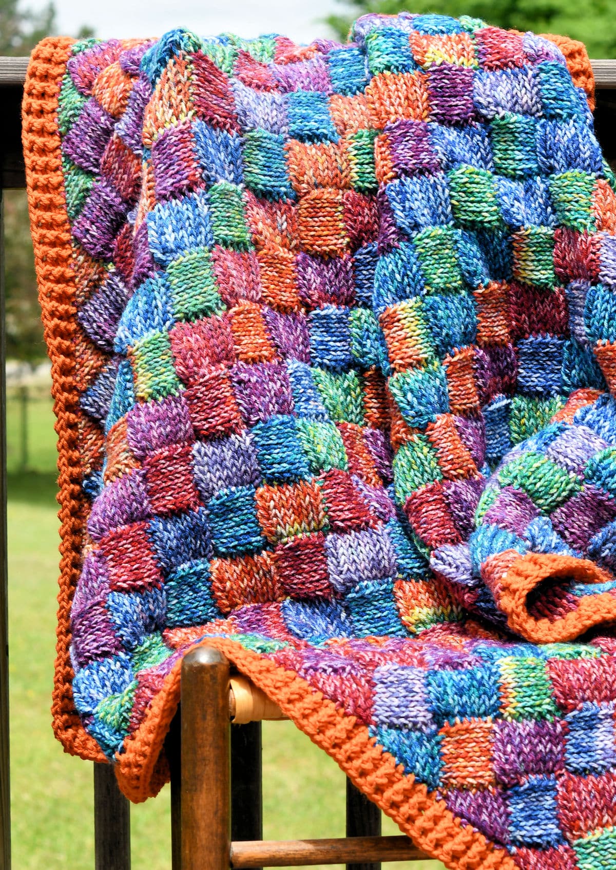 Real knit look crochet entrelac blanket on a cane chair outside.