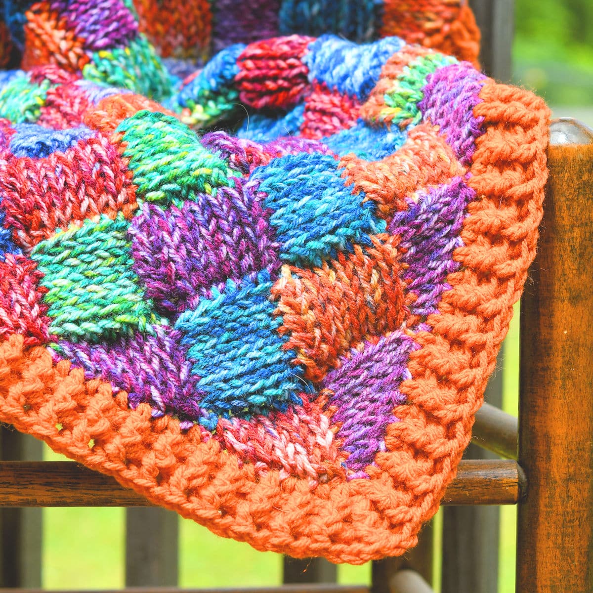 Real knit look crochet entrelac blanket on a cane chair outside.