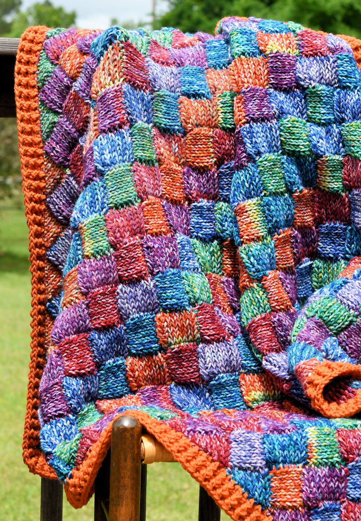 Real knit look crochet entrelac blanket on a cane chair outside.